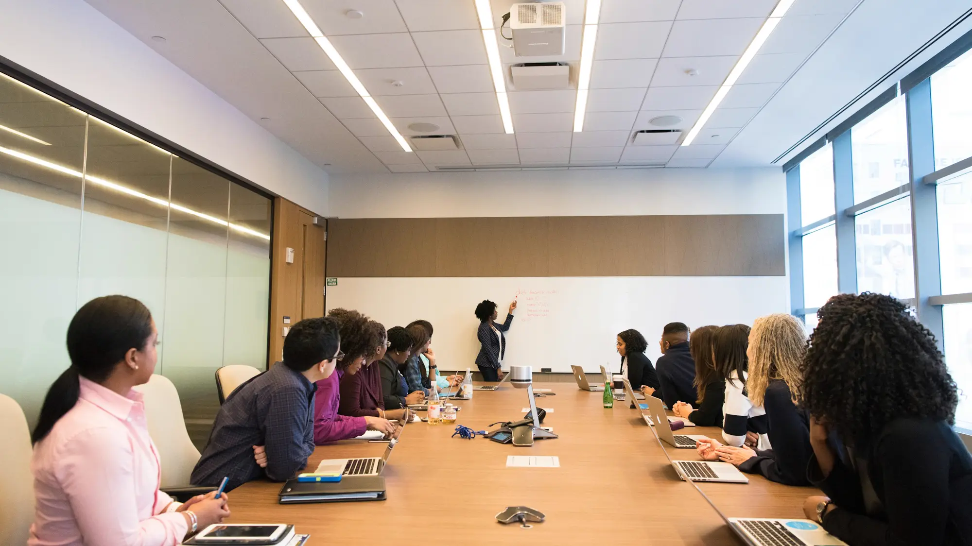 Session de formation en entreprise : un intervenant au tableau et une équipe réunie autour d'une table, ordinateurs ouverts